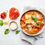 Pasta allo scarpariello: ricetta veloce e cremosa della tradizione napoletana 1 In primo piano un piatto di pasta allo scarpariello con pomodoro, basilico fresco e scaglie di formaggio servito in una ciotola chiara su tovagliolo di lino, con ingredienti freschi come pomodori, peperoncino e formaggio accanto.