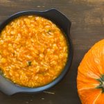 Pastina con la zucca: cremosa, leggera e perfetta anche con il Bimby 1 Pastina con la zucca servita in una ciotola nera accanto a una zucca intera su sfondo in legno.