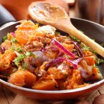 Come cucinare la zucca in padella: ricetta base e varianti con cipolla e croccante 2 Zucca in padella con cipolla rossa, noci e prezzemolo servita in una padella di rame su un tavolo in legno.