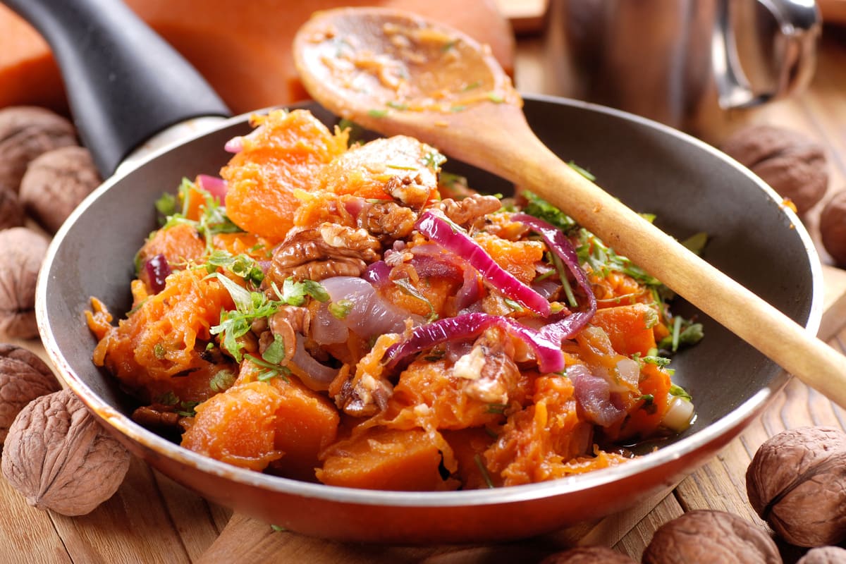 Ricette con la zucca: le migliori idee sane e gustose 10 Zucca in padella con cipolla rossa, noci e prezzemolo servita in una padella di rame su un tavolo in legno.