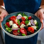 Insalata mista con olio EVO: un contorno leggero che nutre e depura 2 una donna tiene in mano un' insalatiera blu con una bella insalata mista con pomodori oli formaggio e cipolle