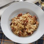 Riso alla pilota: primo piatto tipico della cucina mantovana 1 Riso alla pilota servito in un piatto bianco con salamella mantovana e grana grattugiato sullo sfondo.