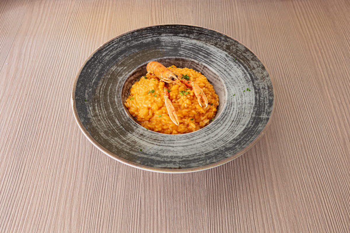 Risotto: ricette semplici e veloci, dai grandi classici alle versioni innovative 4 Piatto di risotto alla crema di scampi servito in un piatto fondo grigio su un tavolo di legno chiaro, con decorazione di prezzemolo fresco.