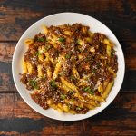 Pasta alla genovese: ricetta del sugo napoletano passo dopo passo 1 su tavolo di legno scuro piatto bianco con la pasta con sugo alla Genovese con cipolle e carne