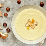 Zuppa di castagne e patate: il comfort food perfetto dell'autunno 1 su piano di lavoro da cucina piatto fondo con una zuppa di castagne, attorno castagne e funghi
