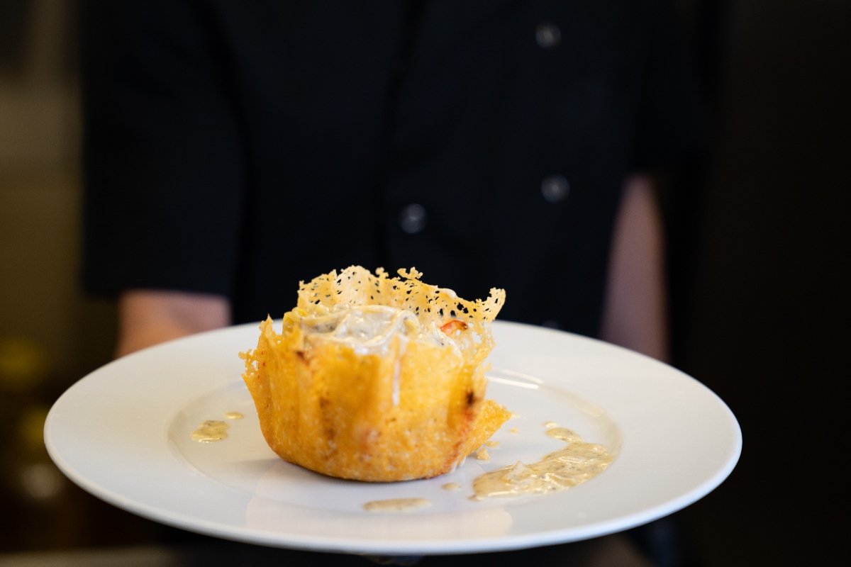 Parmigiano Reggiano: che cos'è, come si fa, benefici, valori nutrizionali e le migliori ricette 6 chef che tiene in mano un piatto bianco e presenta dei cestini di parmigiano con ripieni di formaggio