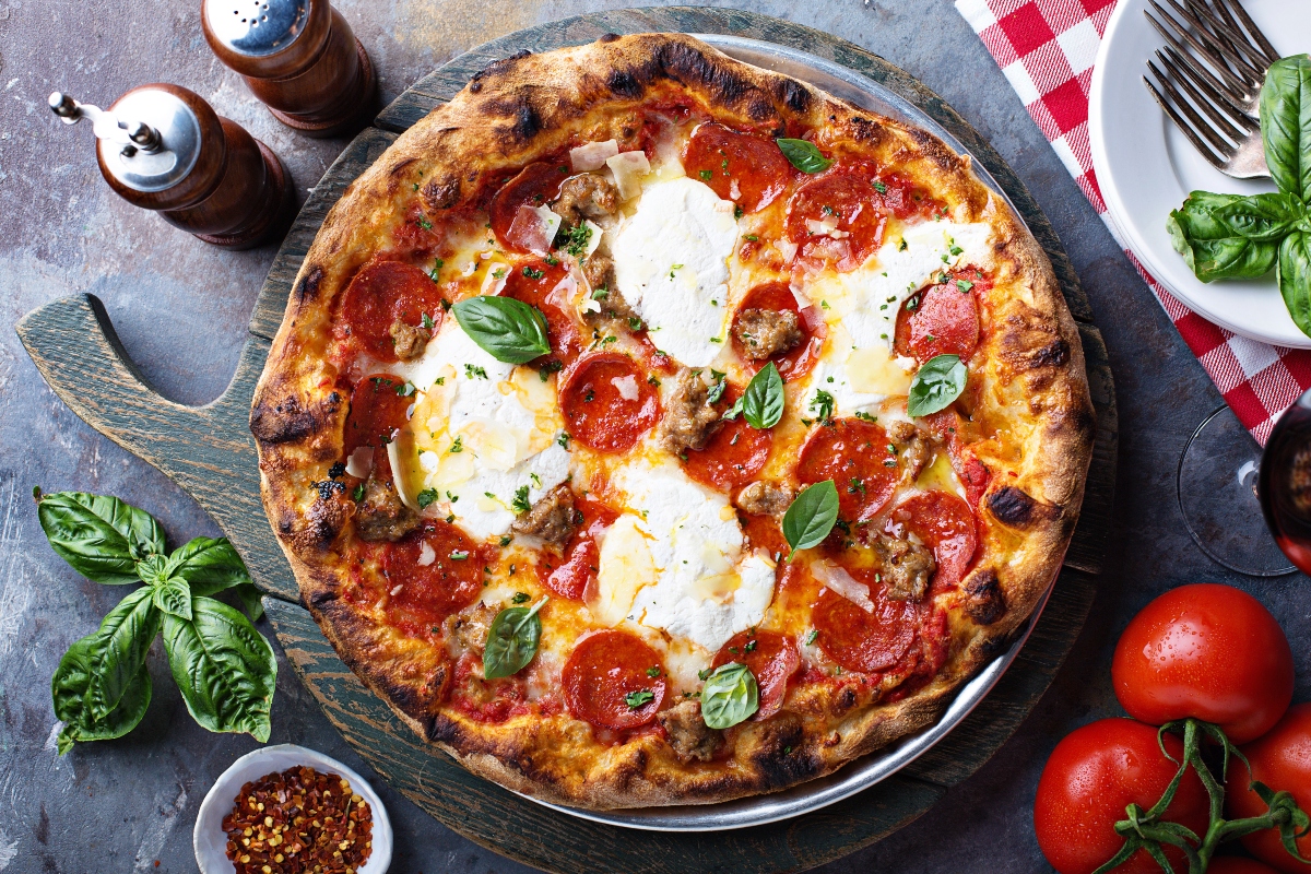 su tavolo nero, tagliere tondo con una pizza margherita e attorno ingredienti come pomodori, basilico, peperoncino