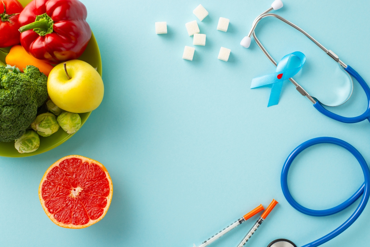 su sfondo blu sulla sinistra alimenti per chi segue una dieta per il diabete e sulla destra stetoscopio, zuccheri e nastro azzurro della giornata mondiale del diabete