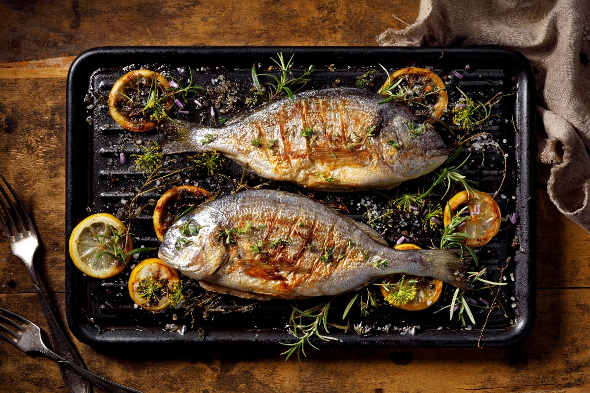 su tavolo di legno, teglia d forno con pesci magri come dentice preparato al forno con fette di limone e erba aromatica