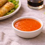 Salsa agrodolce fatta in casa: ricetta facile e veloce 1 in primo piano ciotola con salsa agrodolce cinese e sullo sfondo piatto di involti primavera