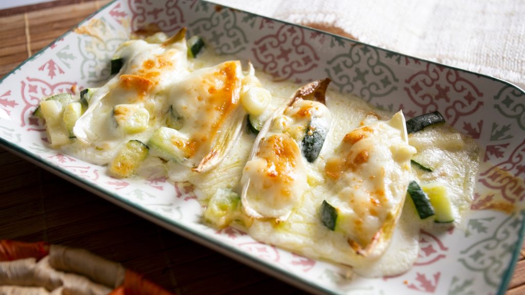 Indivia belga: benefici, proprietà, calorie e come cucinarla (ricette veloci) 2 su tavolo piatto da forno con indivia belga gratinata al forno con besciamella e zucchine