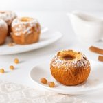 Mele cotte in friggitrice ad aria: ricetta veloce per una merenda sana 1 In primo piano su un tavolo bianco con una tovaglia chiara ci sono delle mele cotte in friggitrice ad aria. Sullo sfondo due stecche di cannella.
