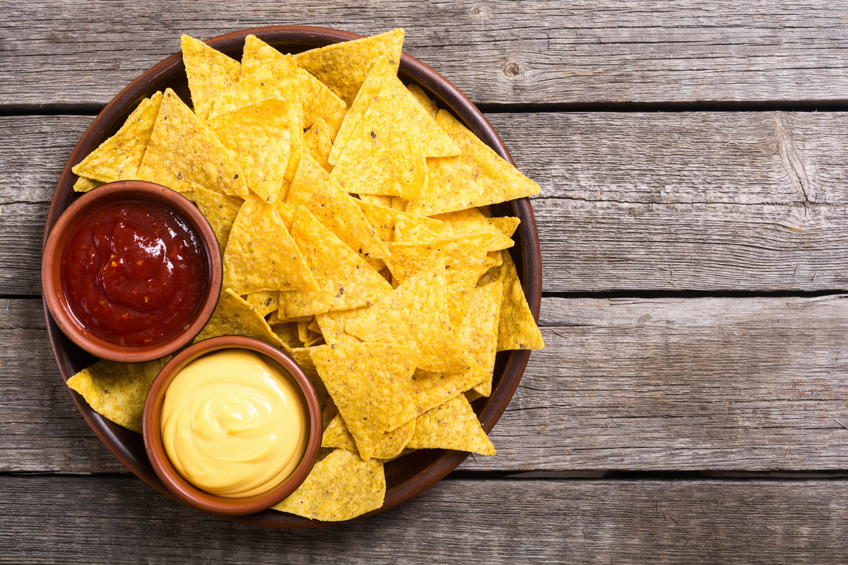 Chips fatte in casa: facili, croccanti e sane 2 su tavolo di legno un piatto tondo pieno di nachos e due ciotole con salsa rossa e gialla