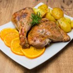 Tacchino al forno: come farlo morbido e succoso 1 su piatto bianco due pezzi di tacchino al forno con patate e fette di arancia