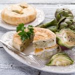 Torta salata con carciofi facile e veloce con video ricetta 1 primo piano sul tavolo di una torta con carciofi tagliata con accanto i carciofi