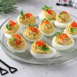 Uova ripiene di tonno: la ricetta senza maionese 1 su tavolo bianco un piatto trasparente con le uova ripiene di tonno e uova di salmone